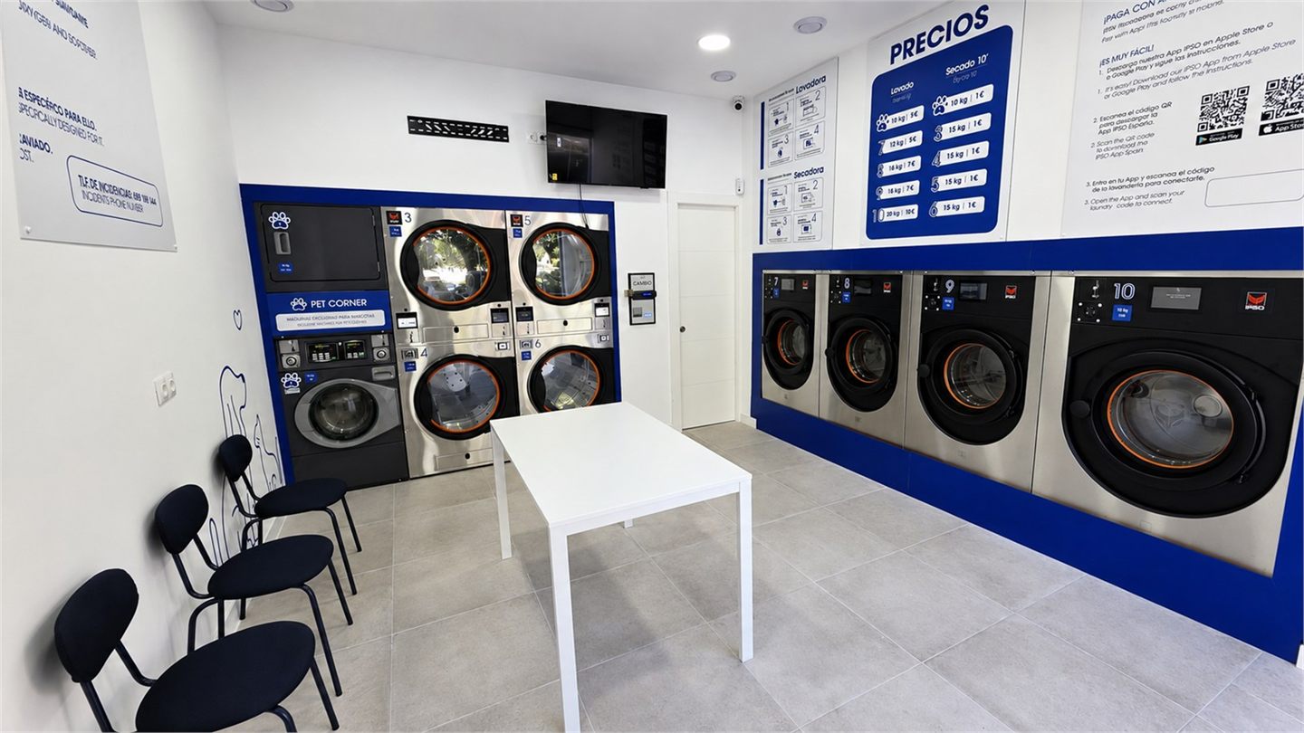 Interior de Washing Day con lavadoras, secadoras, zona de espera y mesa central